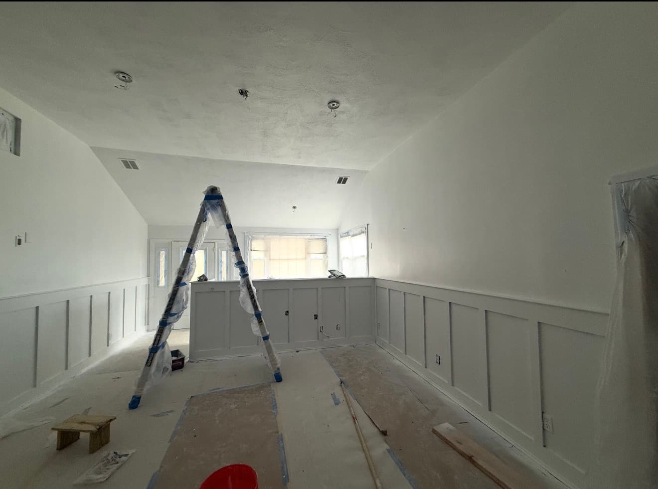 White room renovation featuring board and batten wainscoting, a ladder, and floor drop cloths.