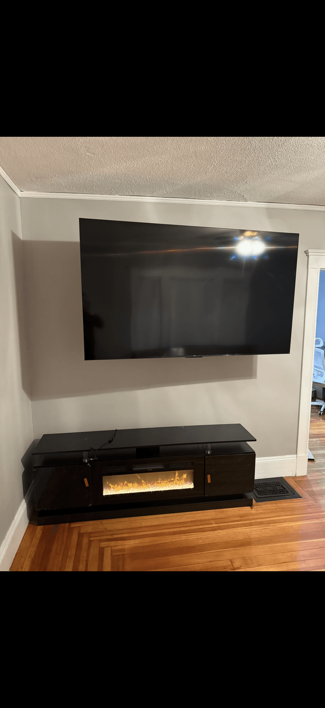Large flat-screen TV mounted on a gray wall above a black electric fireplace console.