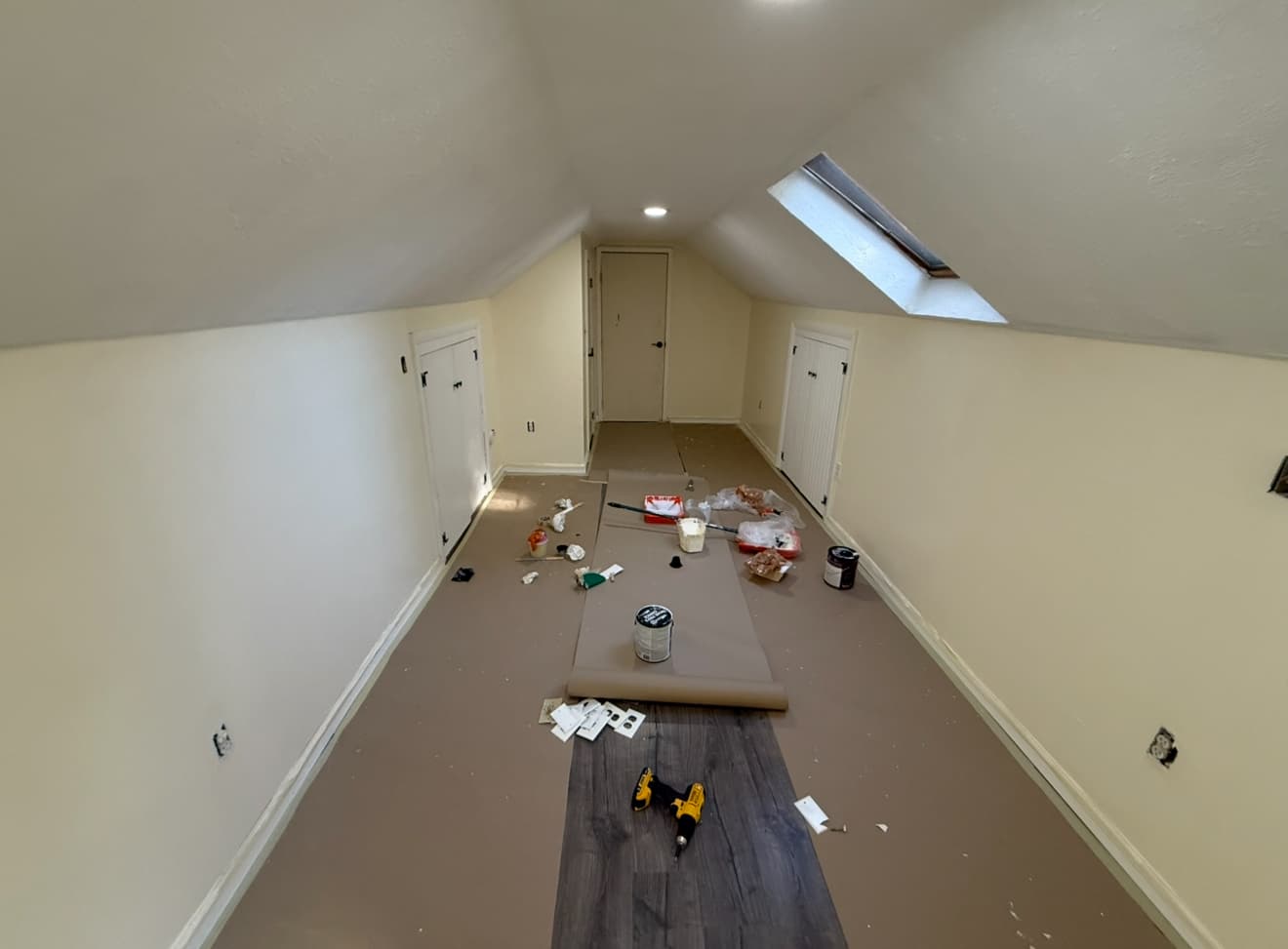 Narrow attic room undergoing renovation with paint supplies and tools scattered across the floor.