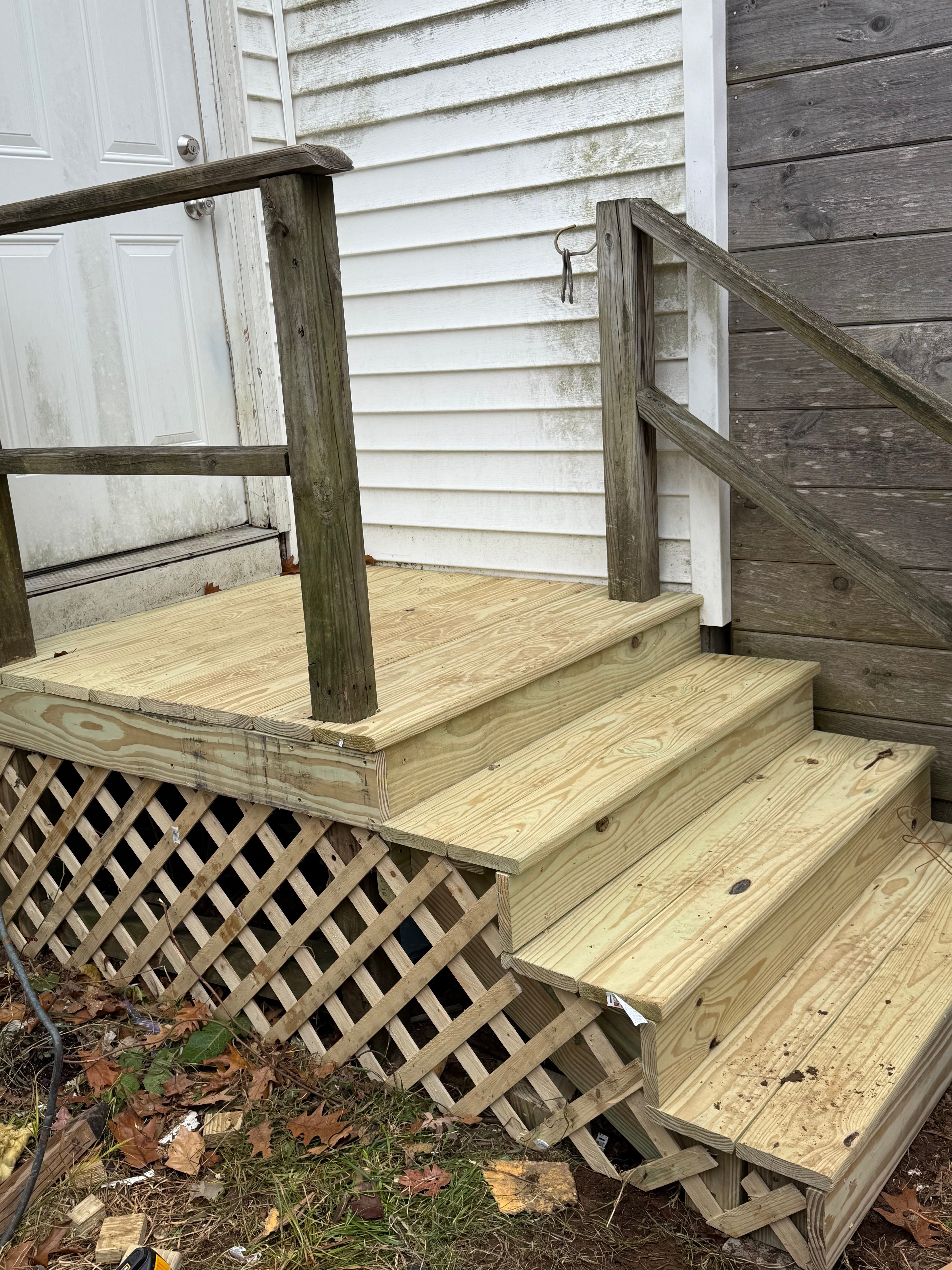 Newly built wooden stairs with lattice skirting next to a white house door.